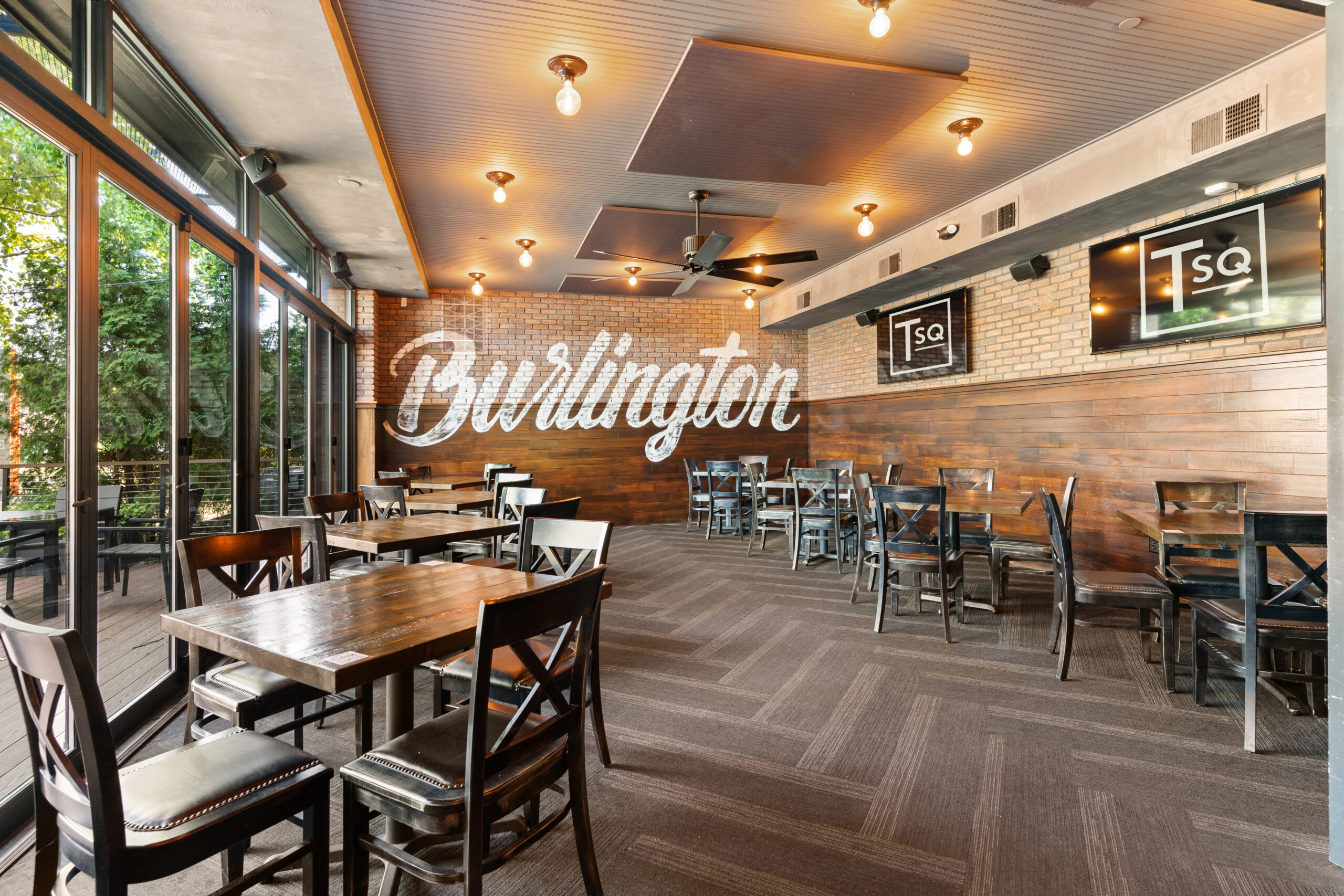 A modern American Tavern dining area with wooden tables and chairs, brick walls, large windows, and 