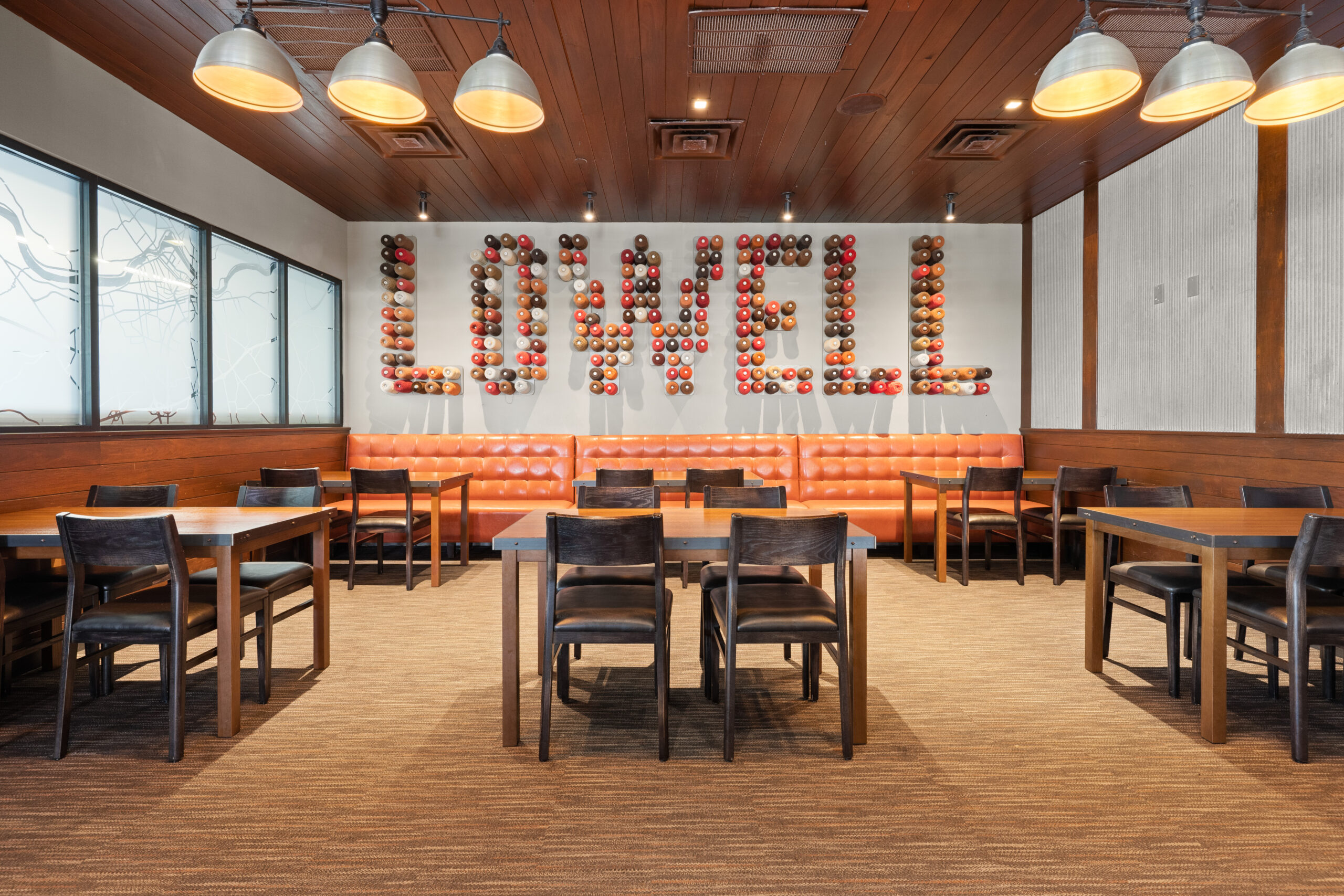A cozy Bar & Restaurant dining area featuring wooden tables and chairs, orange cushioned seating, and a unique wall display spelling “LOWELL” with baseballs—perfect for an authentic American Tavern experience.