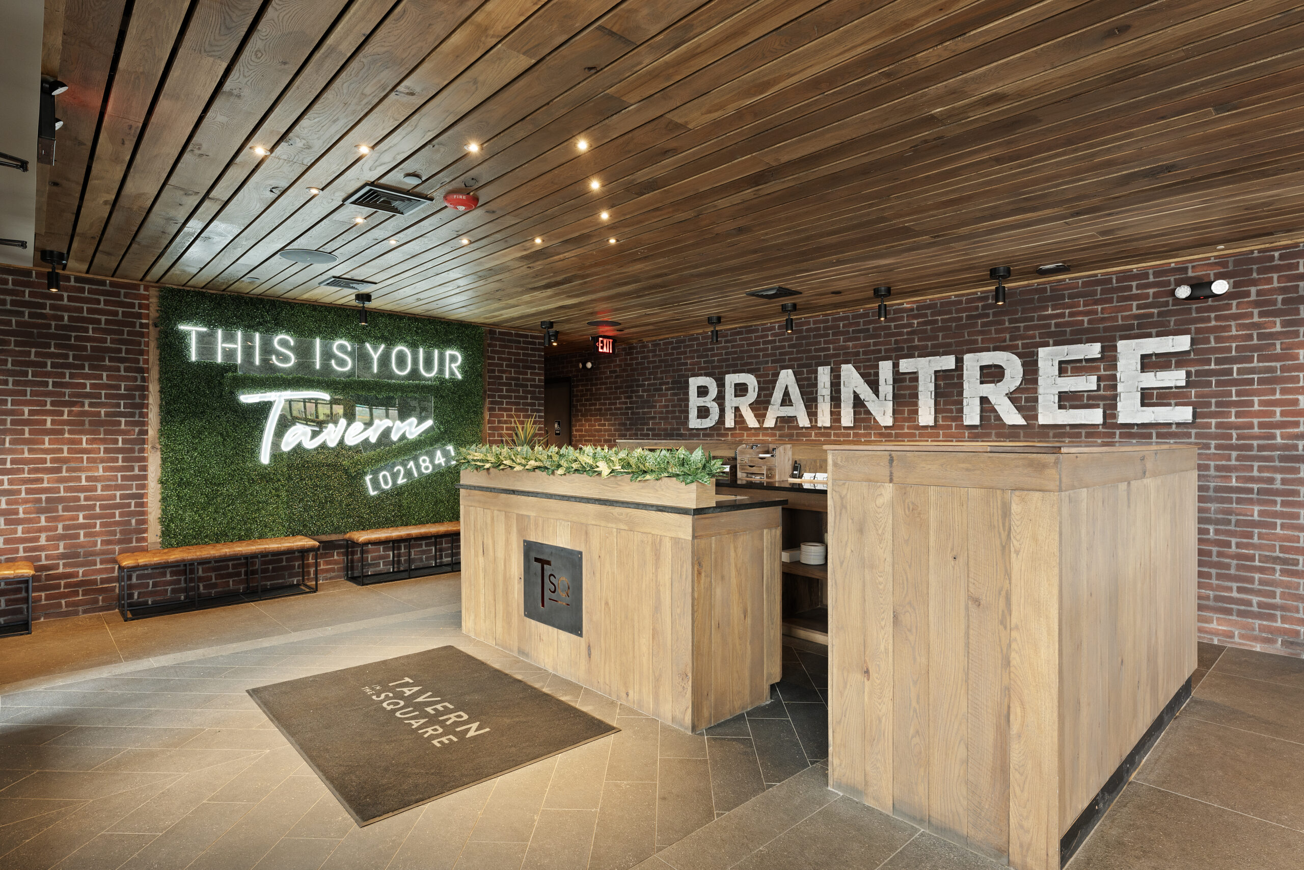 A restaurant entryway with wood paneling, a reception desk, a mat reading 