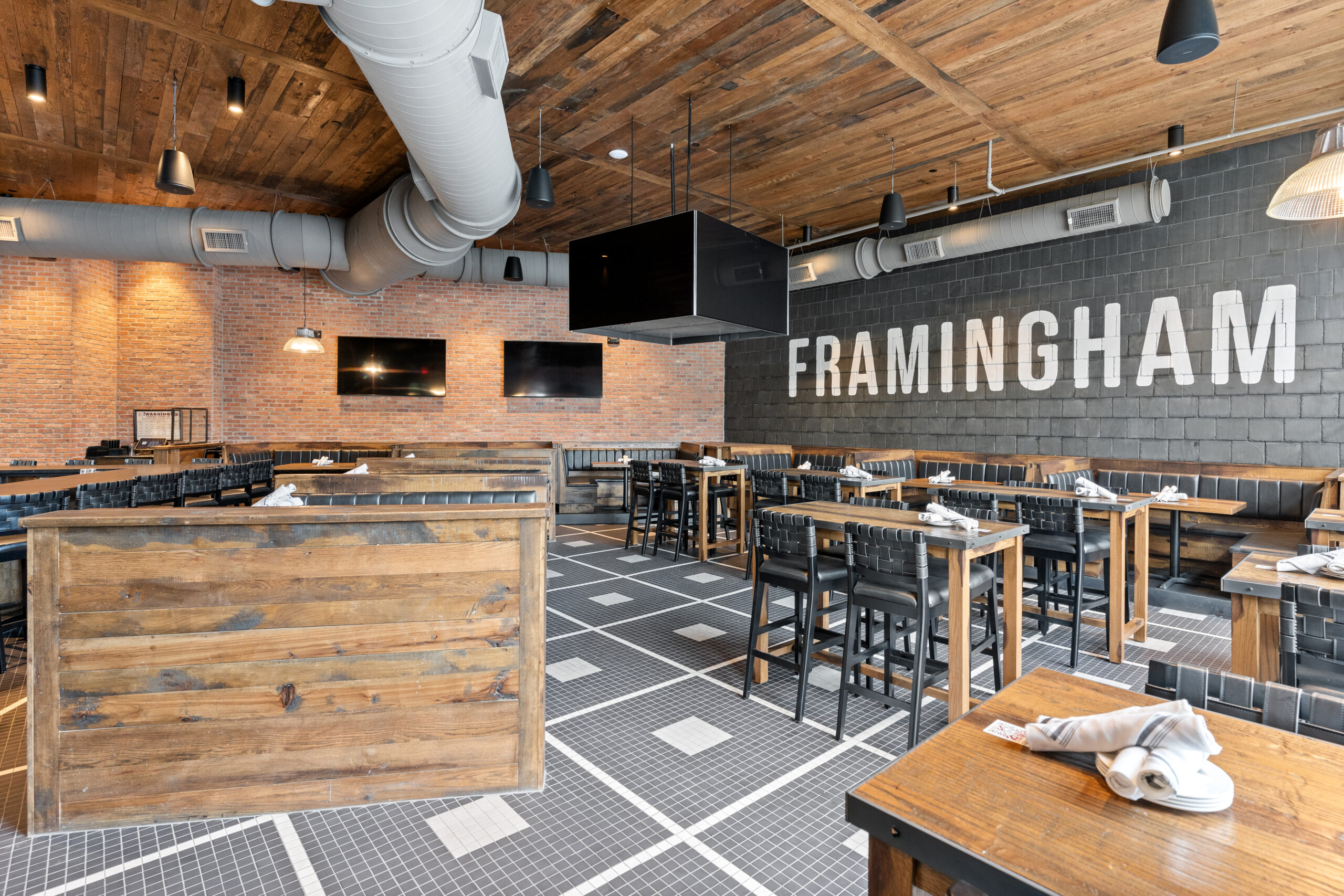 Modern American Tavern interior with wooden tables and chairs, exposed brick walls, industrial ceiling pipes, and 