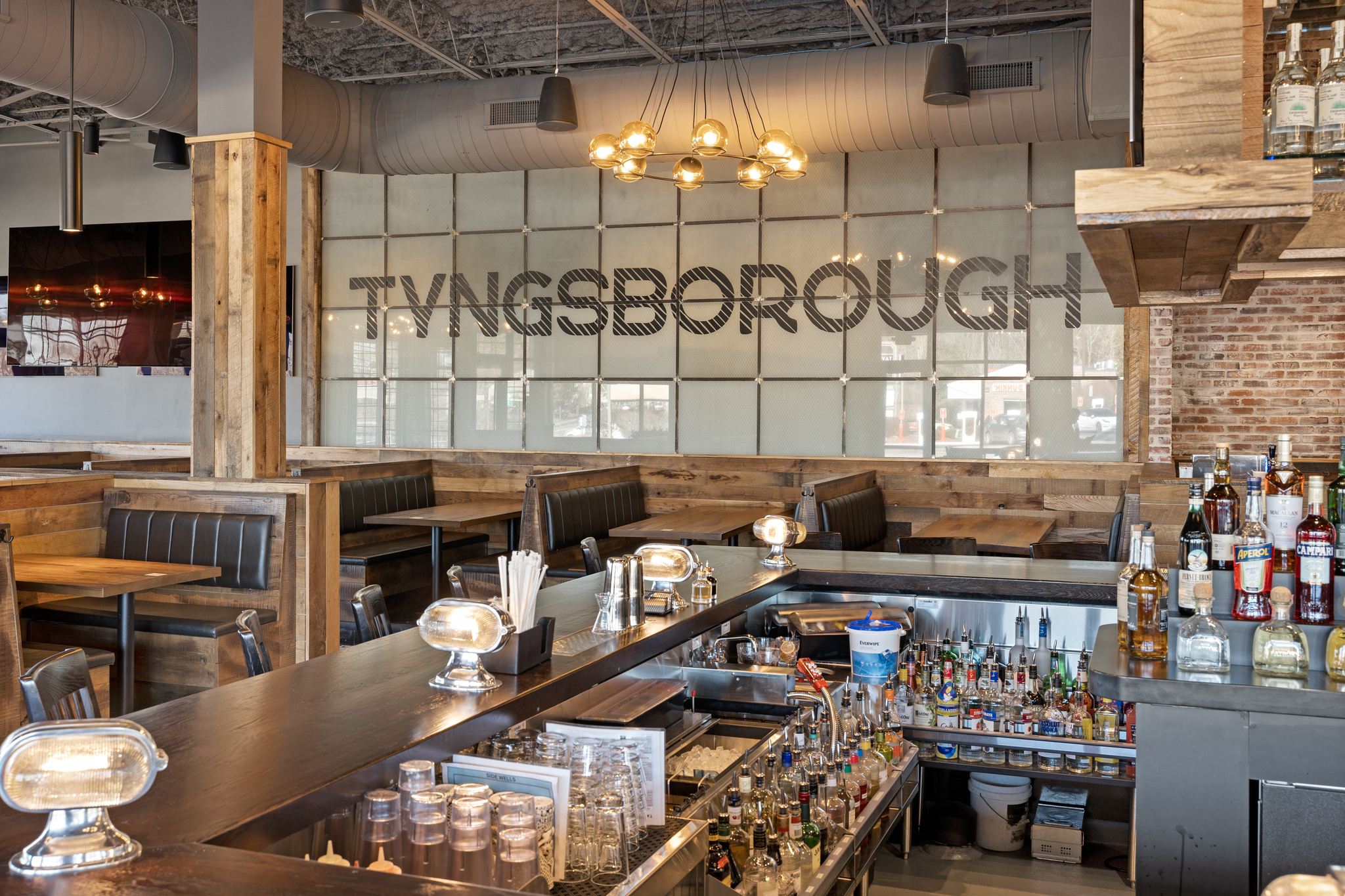 Modern American Tavern bar and restaurant interior featuring wooden booths, a stocked bar, industrial ceiling, and a large 