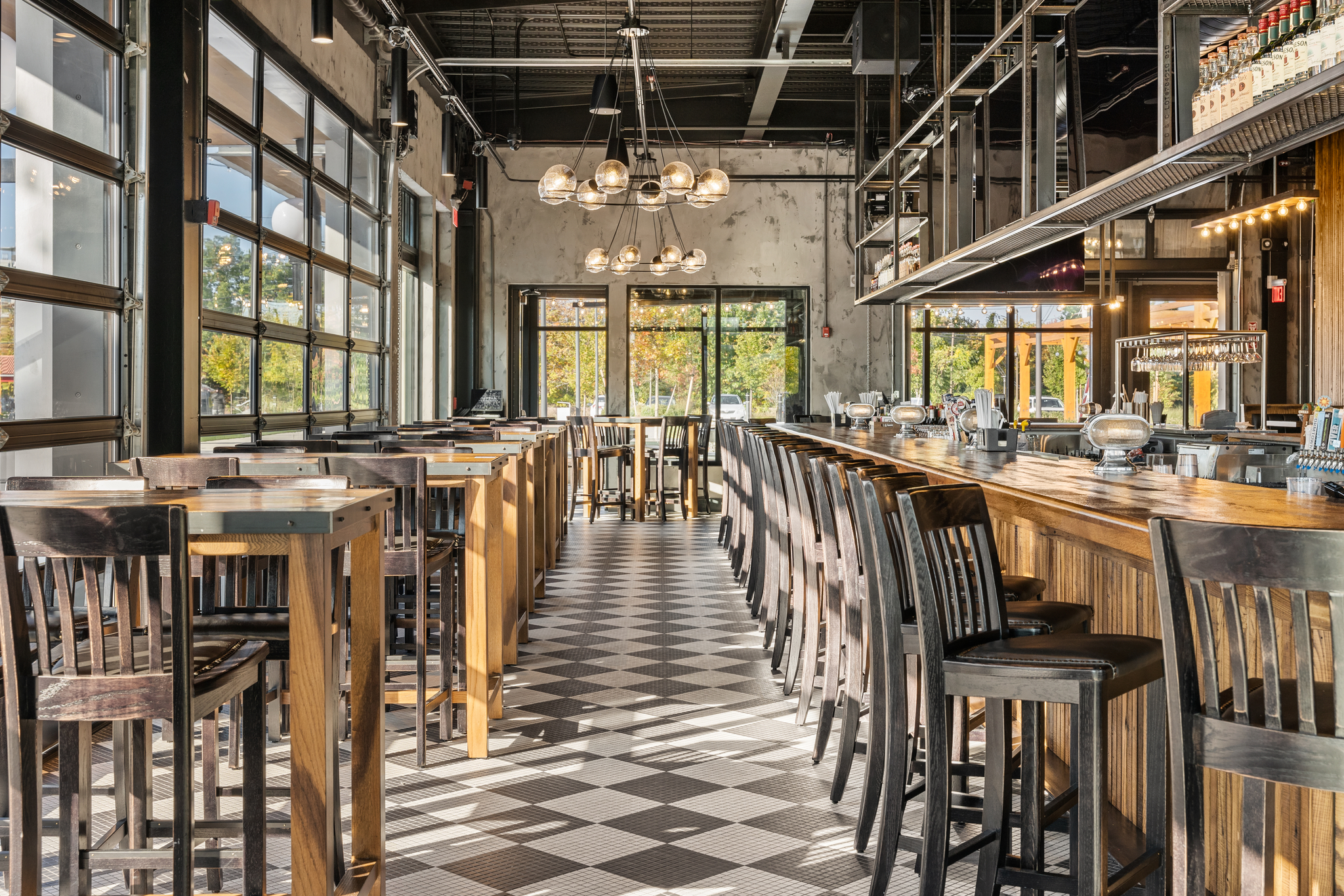 Modern Bar & Restaurant interior inspired by an American Tavern, featuring a checkered floor, wooden tables, high chairs, large windows, and pendant lights, all empty during the daytime.
