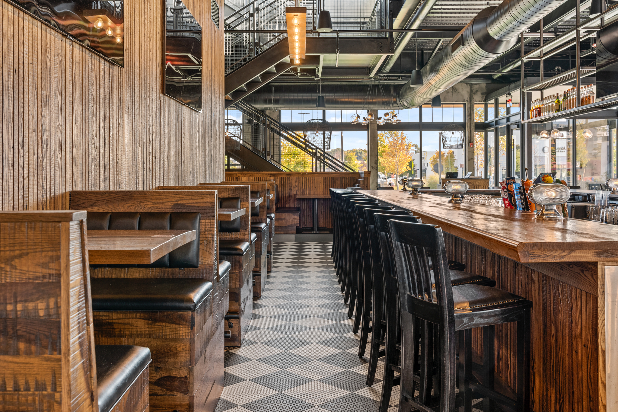 Modern Bar & Restaurant interior featuring wooden booths, a long bar with high chairs, checkered tile floor, and large windows providing natural light for an inviting American Tavern atmosphere.