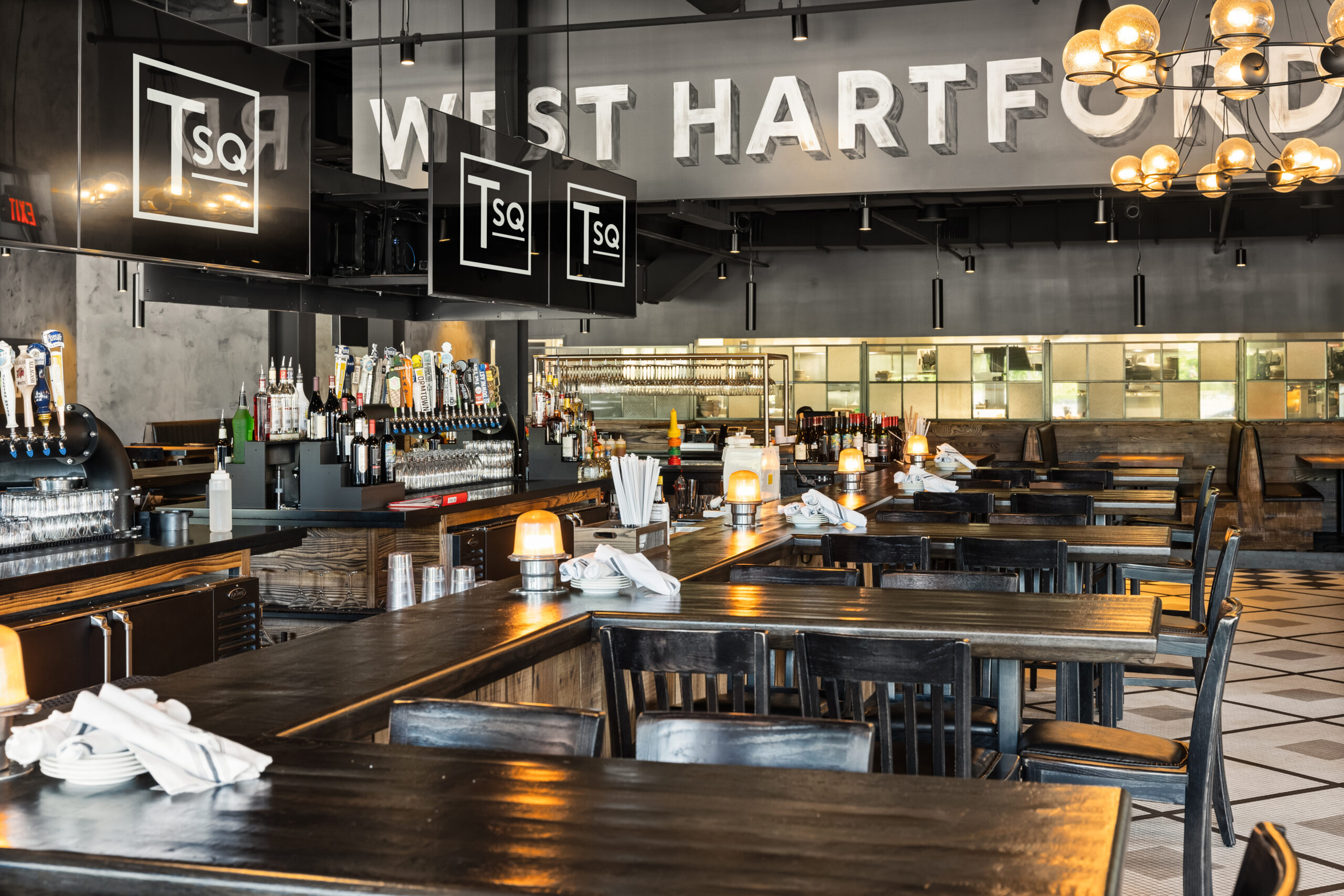 Modern American Tavern interior with wooden tables, bar area, and hanging lights; 