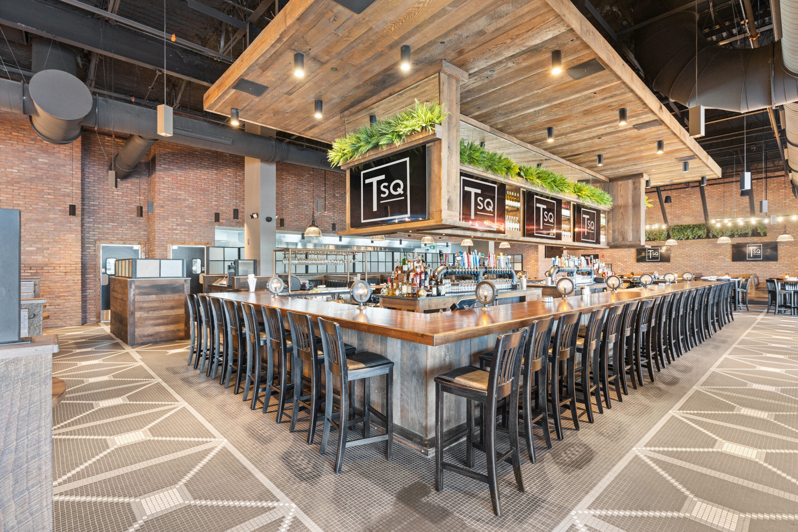 Modern Bar & Restaurant bar area with wooden countertops, black chairs, greenery accents, overhead 