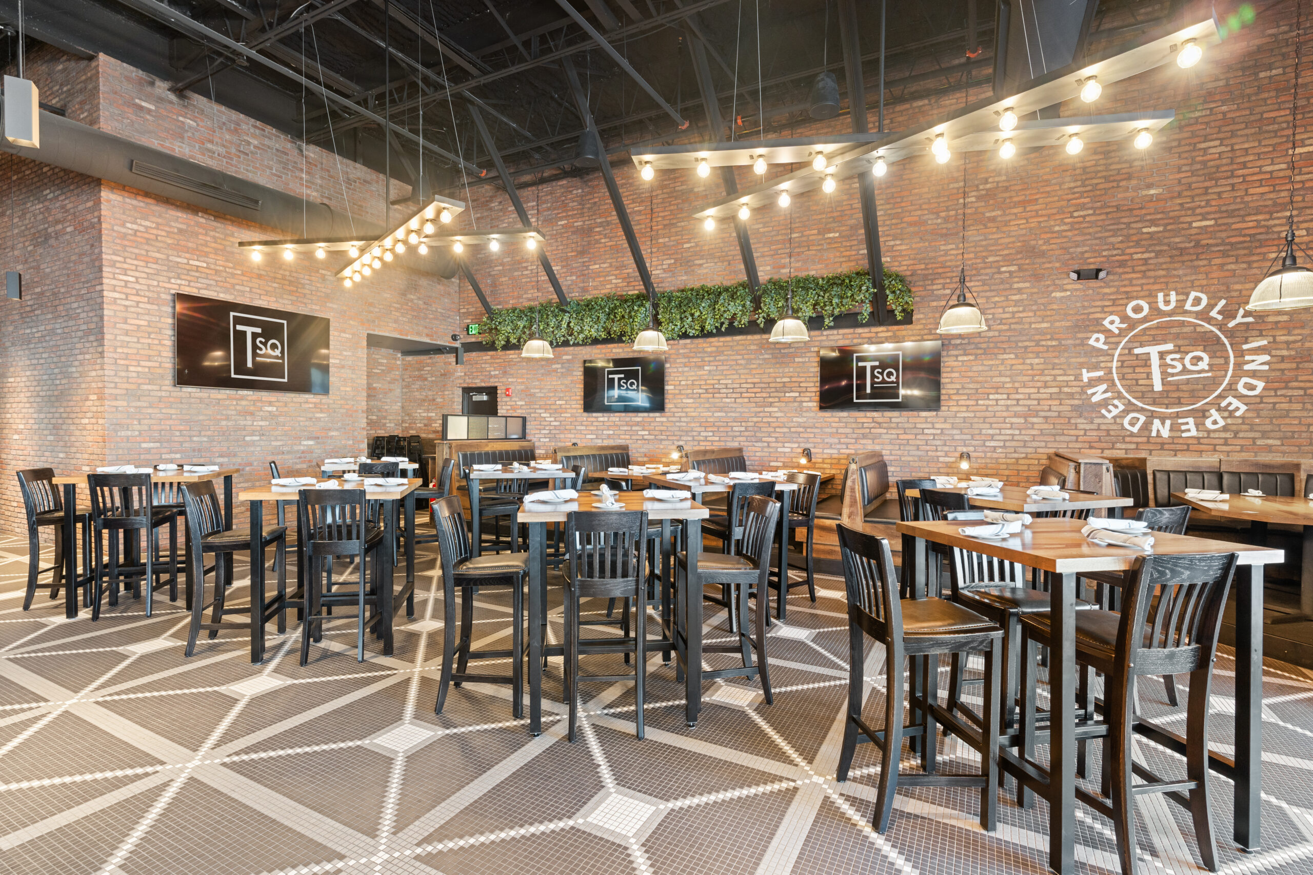 Spacious modern Bar & Restaurant with brick walls, geometric floor tiles, wooden tables and chairs, pendant lights, and green plants above. Multiple Tso logos are displayed on screens and the wall.