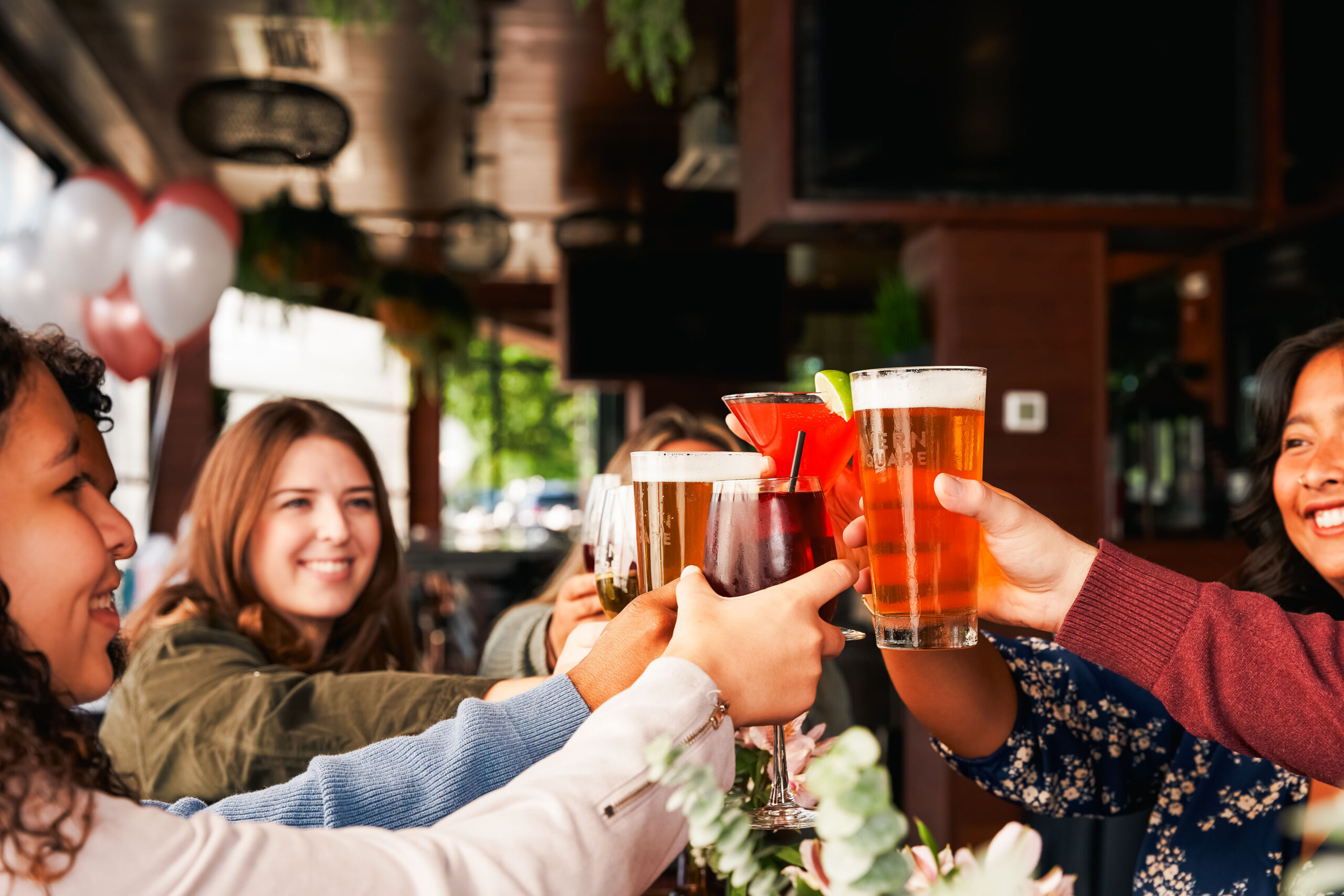 A group of people sit at a table in an American Tavern, clinking beer and cocktails in a lively celebratory toast at the Bar & Restaurant.