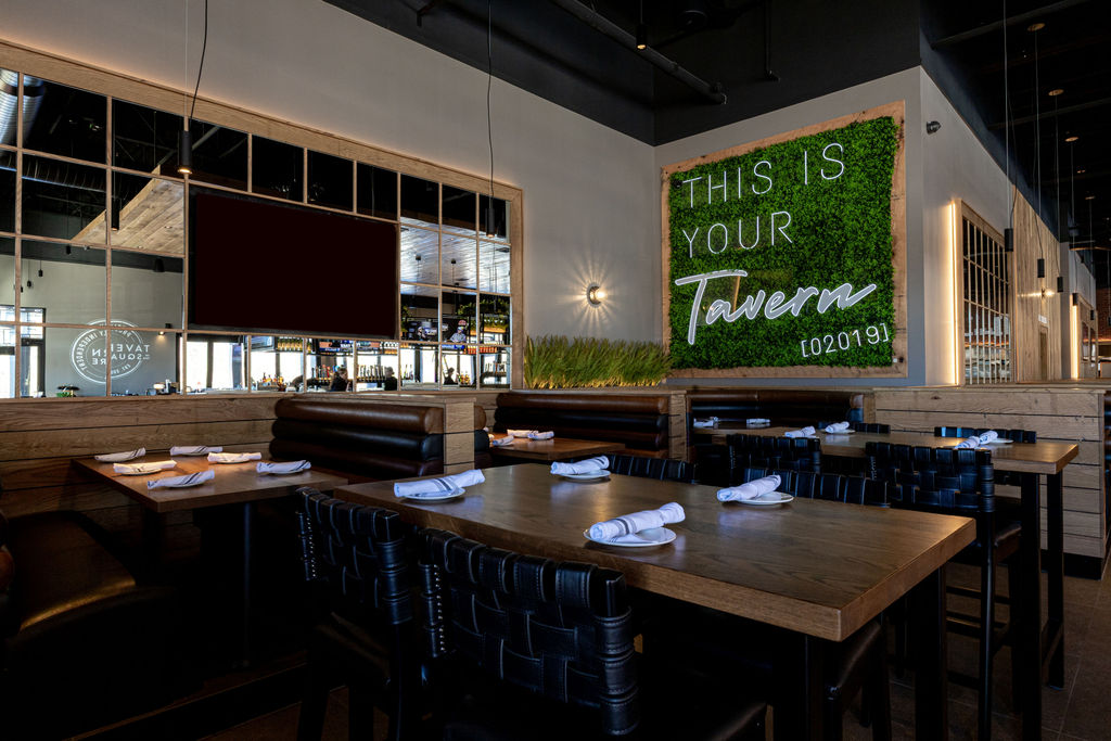 Modern restaurant interior with wooden tables, black leather seating, and a large sign that reads 