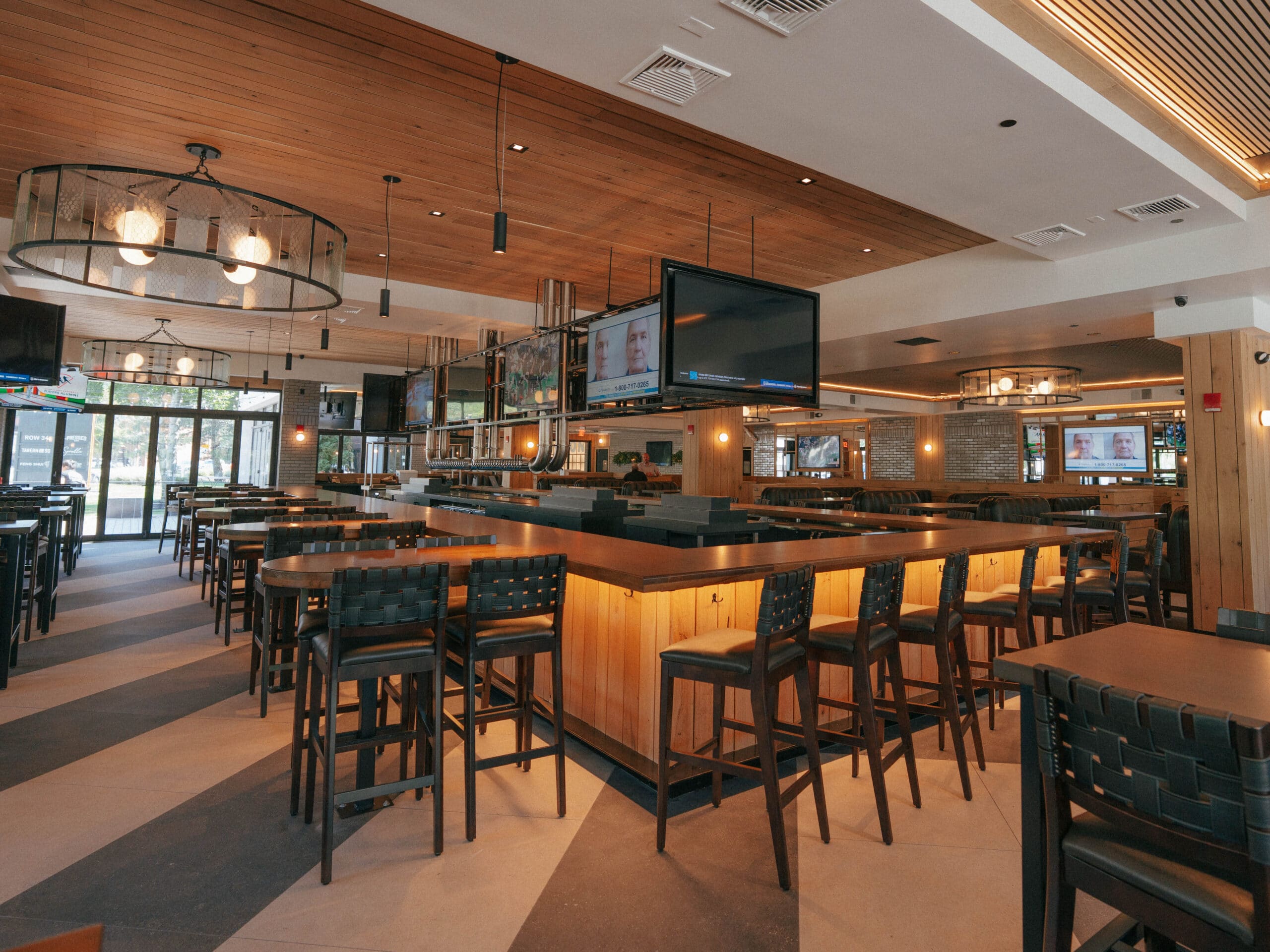 Spacious, modern sports bar in Burlington MA with wooden accents, high tables and chairs, large TVs, and ample natural light from windows.